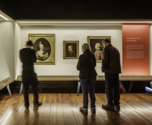 Inside Hampton Court Palace, people viewing one of the showcases displaying contemporary portraits of Capability Brown, the Empress Catherine and King George III